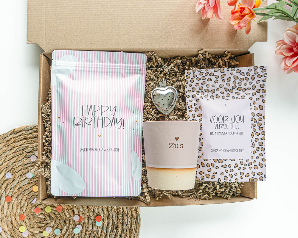 verjaardagscadeau voor haar in roze tinten met daarin een kopje, thee, theezeefje en lekkere snoepjes met opdruk 'happy birthday'.