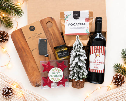 Kerstpakket met wijn, serveerplank, focaccia, pesto en kerstdecoratie