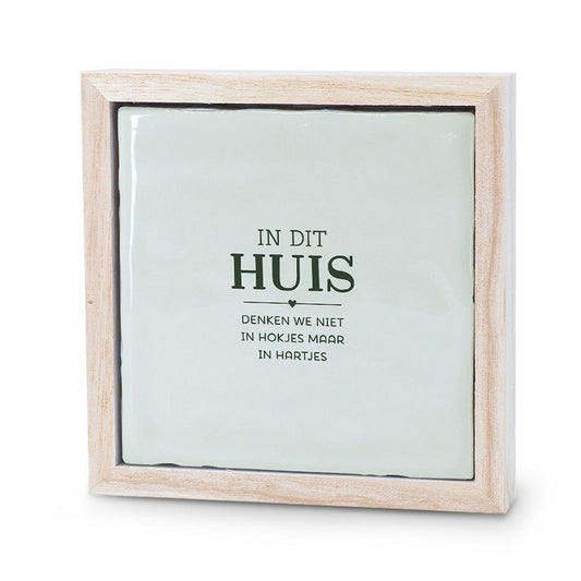 Keramieken tegeltje met houten lijstje en de tekst ‘in dit huis denken we niet in hokjes maar in hartjes’.